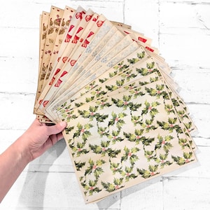 May include: A collection of rectangular paper sheets featuring various vintage-style patterns, including green holly leaves with red berries, red bows, and botanical illustrations on a cream-colored background, fanned out in a stack.