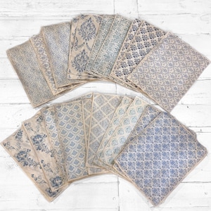May include: A collection of vintage-style paper sheets with various blue floral and geometric patterns. The papers have a distressed, aged appearance, with a beige background and blue designs. The sheets are arranged in a fan shape.