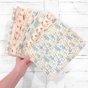 May include: A collection of patterned paper sheets featuring marine life designs. The sheets display various sea creatures like seahorses, turtles, and shells in shades of blue, brown, and orange on a cream background. The paper has a vintage aesthetic.
