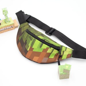 May include: A green and brown Minecraft-themed fanny pack with a black adjustable strap and a zipper closure. The fanny pack has a pixelated design.
