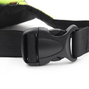 May include: Close-up of a black adjustable buckle on a black nylon strap. The strap is attached to a green and brown camouflage bag.