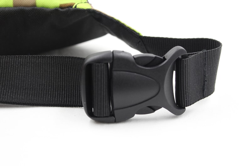 May include: Close-up of a black adjustable buckle on a black nylon strap. The strap is attached to a green and brown camouflage bag.