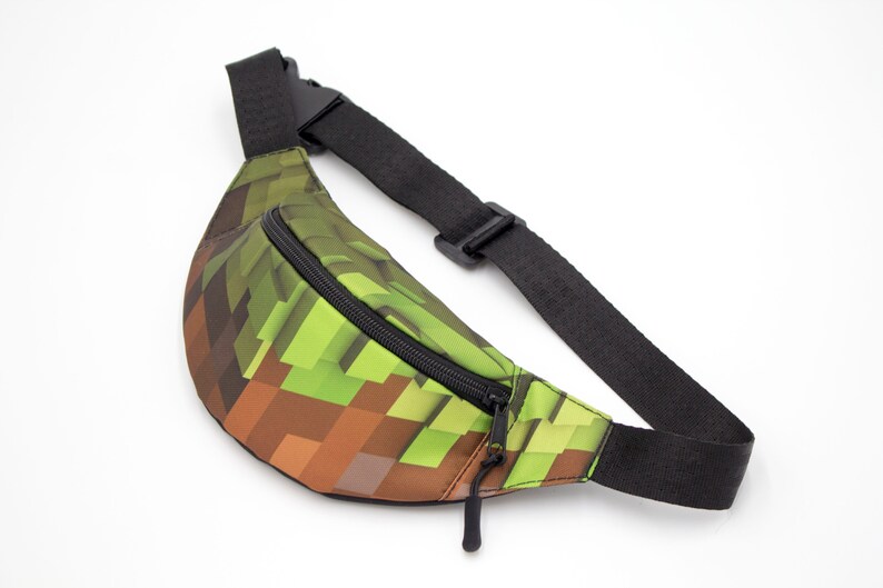 May include: A green and brown pixelated fanny pack with a black adjustable strap and zipper.