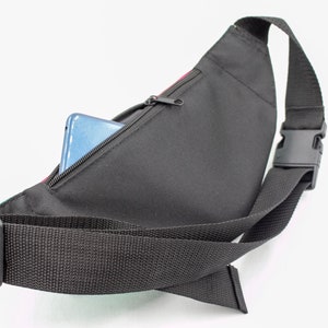 May include: Black fanny pack with a zippered pocket, a black adjustable strap, and a black plastic buckle. A blue smartphone is partially visible inside the pocket. The pack has a colorful accent.