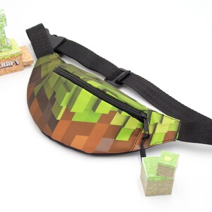 May include: A green and brown fanny pack with a zipper closure and a black adjustable strap. The fanny pack has a Minecraft pixelated design.