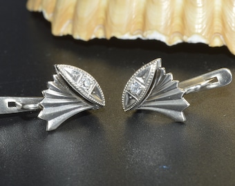 May include: A pair of silver earrings with a fan-shaped design and a small diamond in the center of each earring.