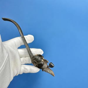 May include: A black wooden pipe with a carved face and a small bowl. The pipe is curved and has a long stem.