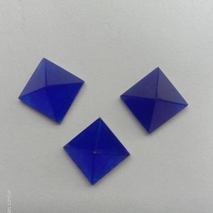 May include: Three blue glass pyramid-shaped embellishments. The pyramids are square and have a smooth, shiny surface.