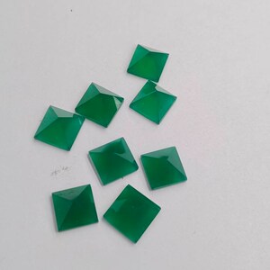 May include: Eight green square pyramid shaped gemstones on a white background.