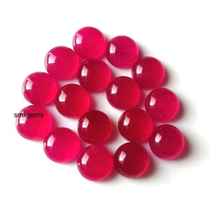 Puede incluir: Un conjunto de piedras preciosas redondas y pulidas de color rojo. Las gemas son de un tono rojo vibrante y tienen una superficie lisa y reflectante. Las piedras preciosas están dispersas sobre un fondo blanco. El texto "smkgems" es visible.