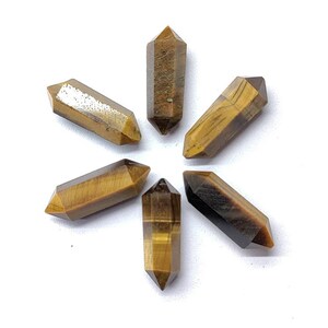 Close up of natural Tiger Eye pencil shape gemstone with golden brown bands and faceted surface