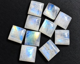 Könnte beinhalten: Eine Ansammlung von neun quadratisch geschliffenen Mondstein-Cabochons, die jeweils eine durchscheinende weiße Basis mit irisierenden blauen und gelben Lichtreflexen aufweisen. Die Steine sind gruppiert und zeigen glatte, polierte Oberflächen.