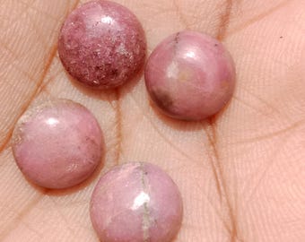 May include: Four round, polished rhodochrosite gemstones in varying shades of pink and rose. The gemstones are smooth and have natural variations in color and texture. The image is taken in natural light, highlighting the stones' luster.