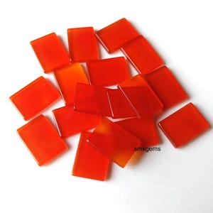 Puede incluir: Una colección de piedras preciosas rectangulares pulidas en tonos naranja y rojo. Las piedras están dispersas sobre una superficie blanca, con diversos grados de translucidez. El efecto general es una exhibición vibrante de piedra natural.