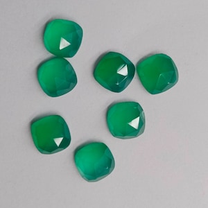 May include: Eight green gemstone cabochons with a faceted cut. The gemstones are arranged in a scattered pattern on a white background.