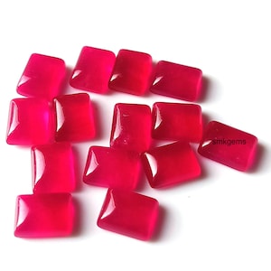 Può includere: Una collezione di gemme rettangolari lucide di un ricco colore rosso. Le gemme hanno angoli arrotondati e una finitura lucida, sparse su una superficie bianca. Il testo "smkgems" è visibile su una delle gemme.