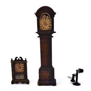 May include: Three antique miniature items: a tall wooden grandfather clock, a small wooden clock, and a black rotary telephone. The clocks have detailed faces and are made of dark wood. The telephone is black with a curved receiver.