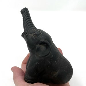May include: A black ceramic elephant figurine with a raised trunk. The elephant is sitting on its haunches with its head tilted up.