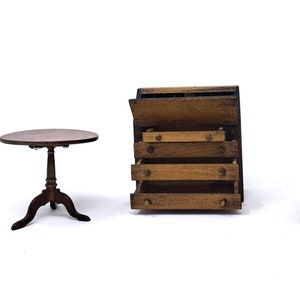 May include: Miniature wooden furniture set, including a round table with a pedestal base, a chest of drawers with four drawers, and a chair with a curved back. The furniture is made of dark wood and is set against a white background.