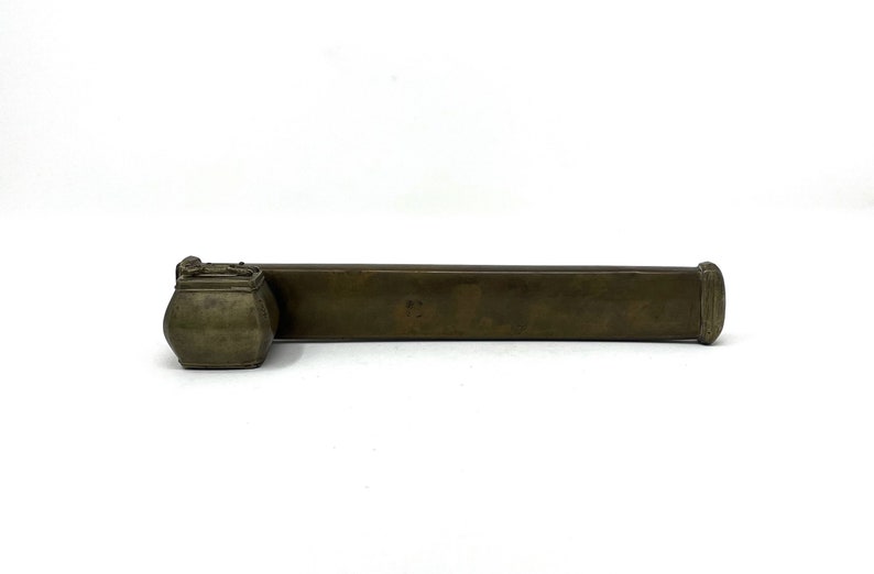 May include: A brass inkwell set with a rectangular container and a round inkwell. The inkwell is attached to the container.