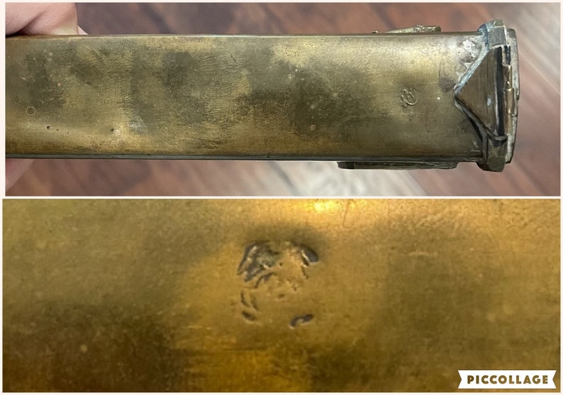 May include: A close-up of a brass, rectangular box with a decorative design on the top. The box has a small, engraved mark on the bottom.