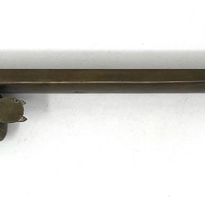 May include: A brass inkwell with a long, rectangular body and a round, hinged lid. The inkwell has a small, round opening on the top for dipping a pen.