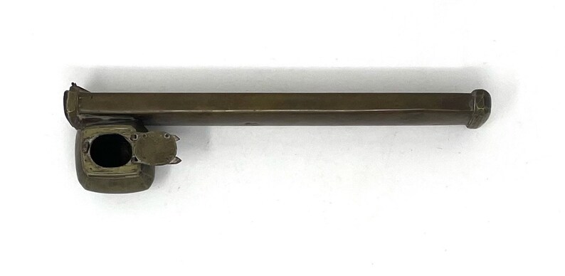 May include: A brass inkwell with a long, rectangular body and a round, hinged lid. The inkwell has a small, round opening on the top for dipping a pen.