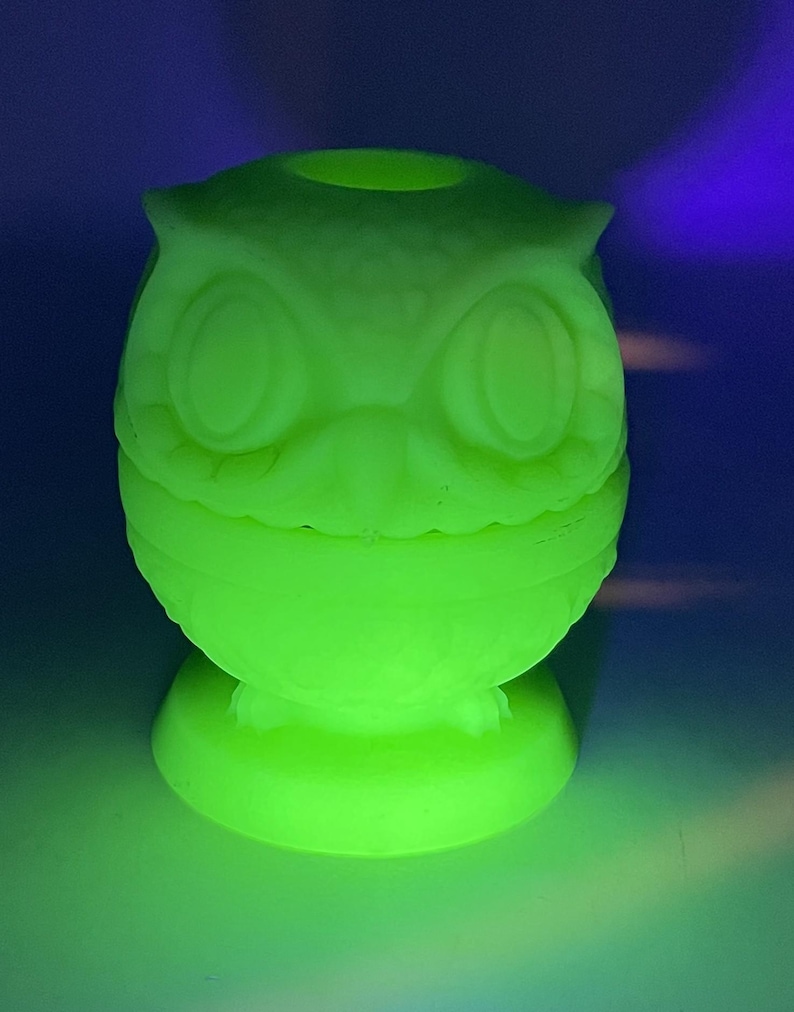 May include: A glowing green owl-shaped figurine. The figurine has large, round eyes, a beak, and ear tufts. It is sitting on a round base. The owl is illuminated with a bright green light, creating a striking visual effect.