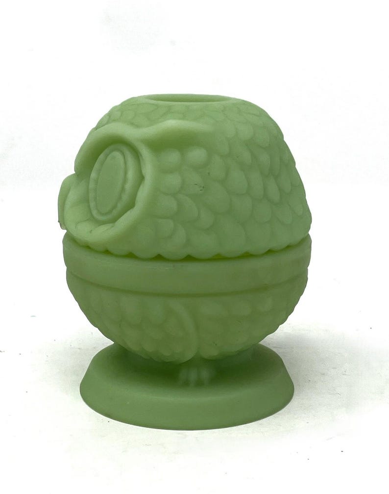 May include: A light green owl-shaped trinket box. The box is made of glass and has a detailed design of an owl's feathers and facial features. The trinket box is approximately 4 inches tall.
