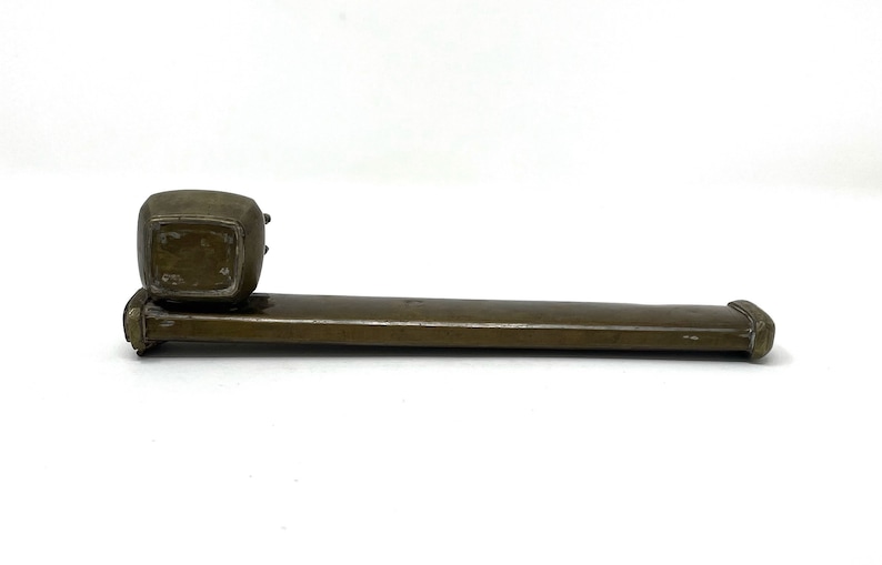 May include: A brown metal inkwell with a square base and a round top. The inkwell is attached to a long, rectangular metal base.