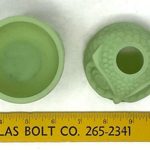 May include: Two light green glass objects. One is a small bowl, the other is a decorative piece with a hole in the center. The objects are next to a yellow ruler with the text "ATLAS BOLT CO. 265-2341".