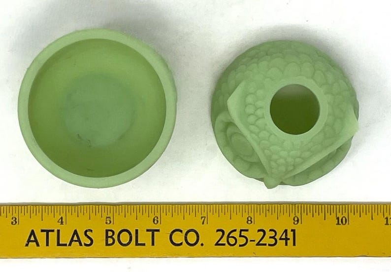 May include: Two light green glass objects. One is a small bowl, the other is a decorative piece with a hole in the center. The objects are next to a yellow ruler with the text "ATLAS BOLT CO. 265-2341".