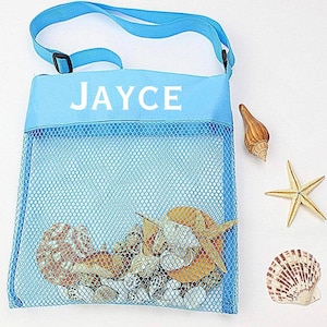 May include: A light blue mesh bag with a blue strap and the name "JAYCE" printed on the front. The bag is filled with seashells and a starfish.