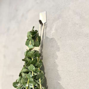 Eucalyptus bundle hanging in the shower with a close up of the adhesive hook used to hold the bundle on the wall.