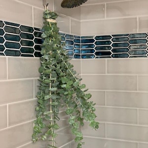 A shower eucalyptus bunch hanging in a tiled shower that is beige and mermaid tiled.