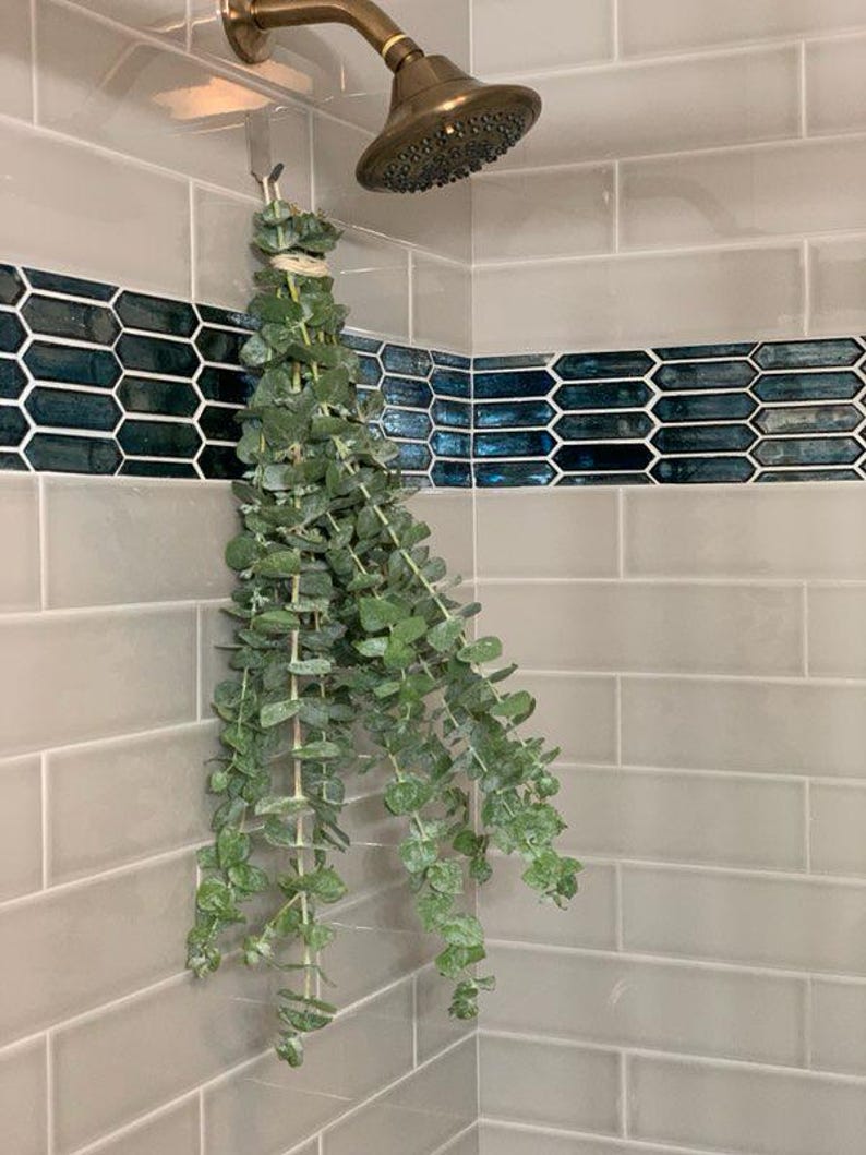 A shower eucalyptus bunch hanging in a tiled shower that is beige and mermaid tiled.