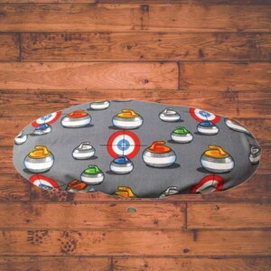 May include: Grey fabric with a repeating pattern of curling stones. The stones are red, yellow, blue, and green. The stones have a bullseye target on them.
