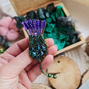 May include: A purple and green beaded flower brooch with a long beaded chain.