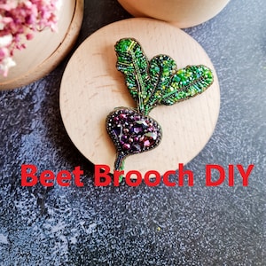 May include: A beet brooch DIY project, featuring a beaded beet with a green leafy top, on a wooden surface. The text "Beet Brooch DIY" is written below the brooch.