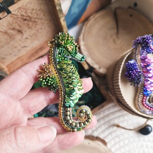Puede incluir: Un broche de caballito de mar de cuentas verdes y doradas. El caballito de mar est&aacute; hecho de cuentas verdes y doradas y tiene un dise&ntilde;o detallado.