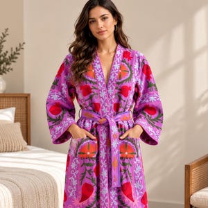 Peut inclure: Une robe de chambre longue à manches longues, de couleur violette vive, ornée d'une broderie florale et de grenades dans des tons rouge, orange et vert. Le vêtement comprend une ceinture à nouer assortie et deux poches avant.