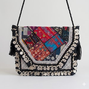 Peut inclure: Un sac à bandoulière patchwork coloré avec une sangle et une garniture noires. Le sac présente une variété de tissus à motifs rouges, bleus et autres couleurs, agrémentés d'ornements argentés et de breloques en forme de pièces.
