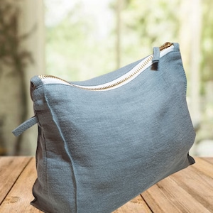 May include: A light blue canvas zippered pouch with a white zipper pull and gold zipper teeth. The pouch is sitting on a wooden surface.