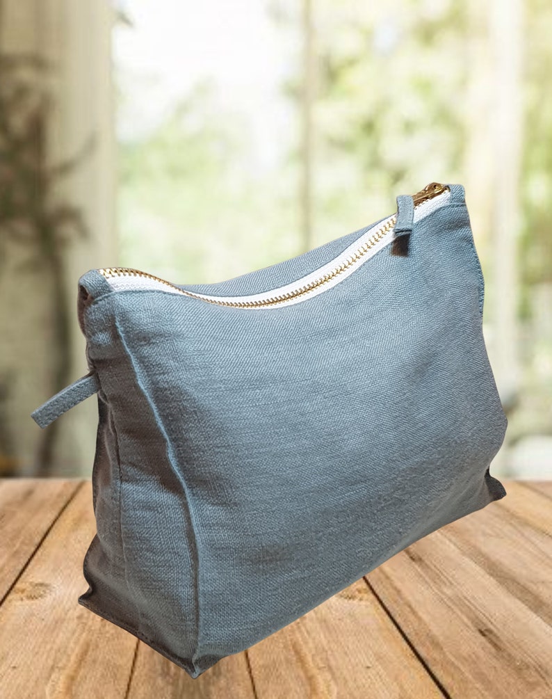 May include: A light blue canvas zippered pouch with a white zipper pull and gold zipper teeth. The pouch is sitting on a wooden surface.