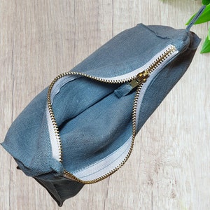 May include: A gray linen zippered pouch with a gold zipper. The pouch is open and the lining is white.