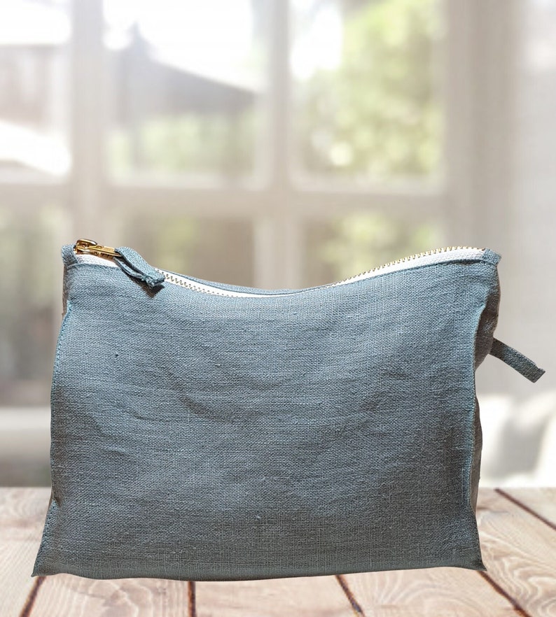 May include: A light blue zippered pouch made of linen fabric. The pouch is sitting on a wooden surface.