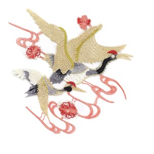 Peut inclure: Patch brodé représentant deux grues grises et blanches avec des accents dorés et roses. Les grues volent les ailes déployées. Le patch présente un motif floral rose avec un motif en spirale.