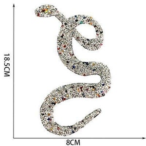 Pode incluir: Uma aplicação de cobra de strass prateada com strass coloridos. A aplicação mede 8 cm de comprimento e 18,5 cm de largura.