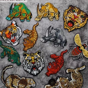 Può includere: Un set di 12 toppe da stirare con diversi animali, tra cui tigri, rinoceronti, un'ape e un leopardo. Le toppe sono realizzate in tessuto colorato con paillettes e dettagli ricamati.