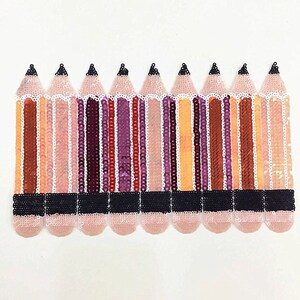 May include: A row of ten colorful pencils made of sequins. The pencils are pink, orange, brown, purple, and red. The pencils have black erasers.